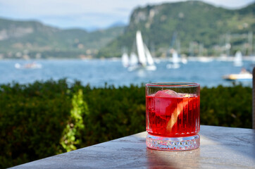 Campari cocktail in a glass on a table, blurred lake and mountains background