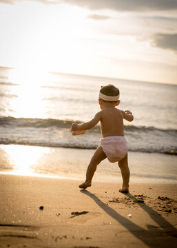 A Baby Girl Running Towards Teh Sea On The Beach During Sunset. 