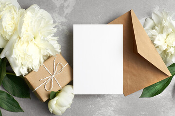 Card mockup with copy space, flat lay with white peony flowers, gift box and envelope on grey