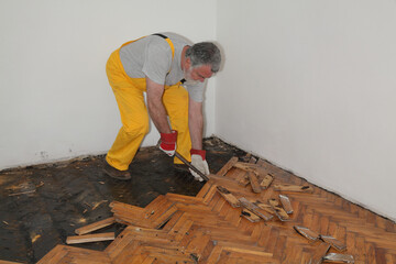 Worker removing old damaged parquet using crowbar tool