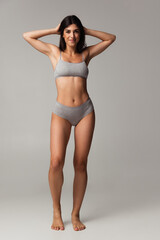 Fototapeta premium Portrait of young beautiful slim woman in lingerie posing isolated over gray studio background. Natural beauty concept.