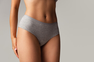 Beautiful body of young caucasian woman in grey lingerie isolated on gray studio background. Natural beauty concept. Bottom view