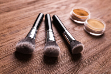 Loose compact mineral powder for face and a brushes for powder and visage on wooden background. Eco...