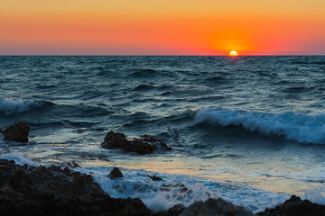 Sunset and storm at sea. Big waves against the setting sun. A summer storm in the ocean. Beautiful sea spray with foam breaks on the rocky shore. Beautiful natural background. The orange setting sun.