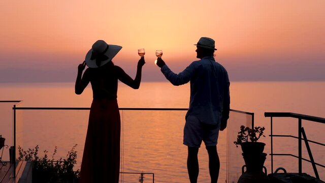 A couple on summer holidays enjoys the summer sunset view over the mediterranean sea with a glass of wine