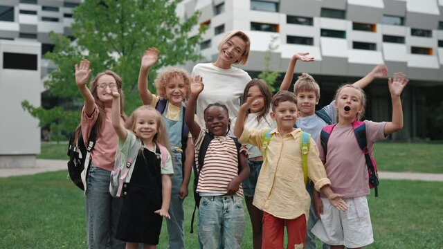 Teacher with children smiling and waving hands on schoolyard