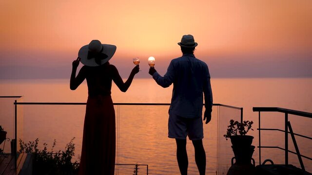A romantic couple enjoys the summer sunset view over the mediterranean sea with a glass of aperitif during their holidays
