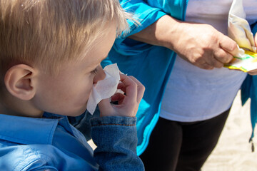 A blond boy holds a napkin near his nose when sneezing. Selective focus.