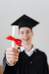 Education, graduation and people concept - happy male student with diploma at home showing his...