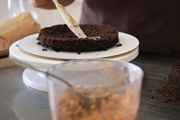 Woman pastry chef impregnates chocolate sponge cake on stand, close-up. Cake making process, Selective focus