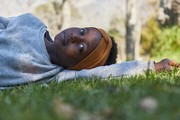 Pretty young black girl lying on grass in grey tracksuit.