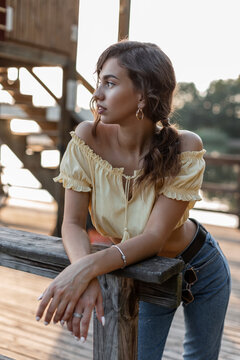 Beautiful curly woman in denim clothes with summer yellow top blouse and jeans stands and rest on a wooden pier