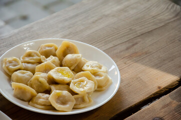 Plate with dumplings stands on wooden table. Rural still life. Homemade ravioli served in white platter on wooden surface with copy space. Delicious meal concept.