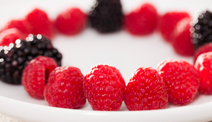 raspberries and blackberries laid out on a white plate in circle