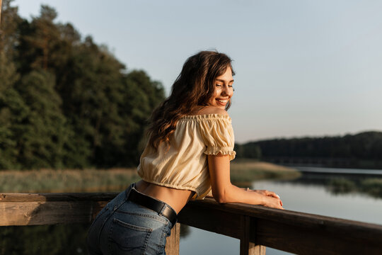 Happiness pretty smiling girl in fashion summer jeans clothes stands on the pier on nature near a lake