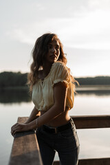 Pretty woman in fashionable blue jeans and a yellow top on nature near a lake at sunset