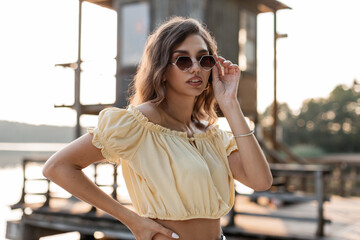 Stylish young beautiful hipster woman put on fashionable sunglasses and resting on the beach by the...