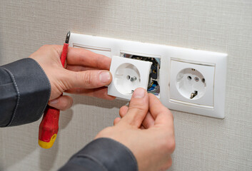 Electrician in uniform assembling electrical outlets on a white wall in a room. Electrician fixing...