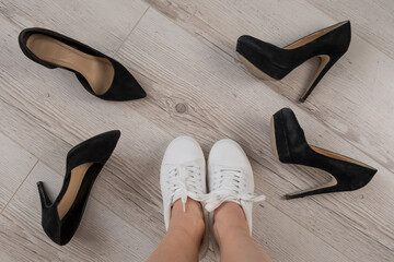 A woman chooses sports shoes instead of high-heeled shoes. Sneakers or shoes
