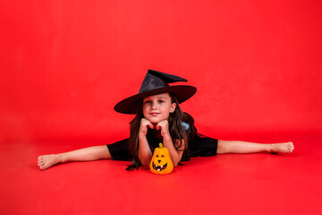 a little girl in a witch costume and with a hat is sitting on a string with a pumpkin on a red...
