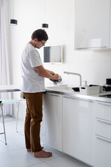 Man in white t shirt washing dishes in the kitchen