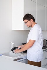 Man in white t shirt washing dishes in the kitchen