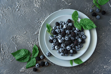 Fresh blueberries and blackberries decorated green leaves on gray concrete background. Top view