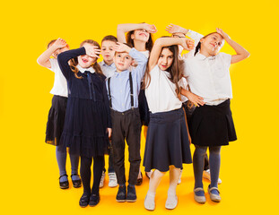 Schoochildren with backpacks and crossed hands standing over yellow background