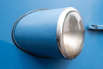 Closeup of a vintage train headlight with a chrome trim on blue surface
