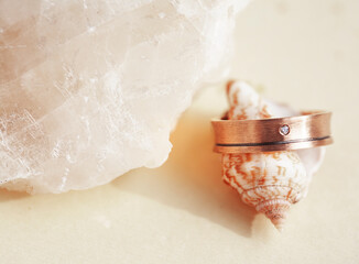 beautiful macro shot of golden wedding ring with sea shell and coral on yellow background