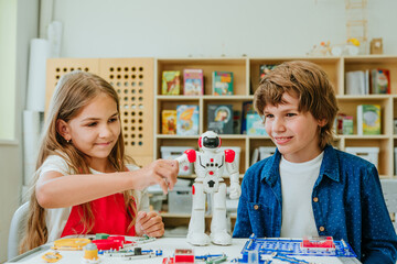 Teenage boy and girl play with robot during a lesson in the classroom.