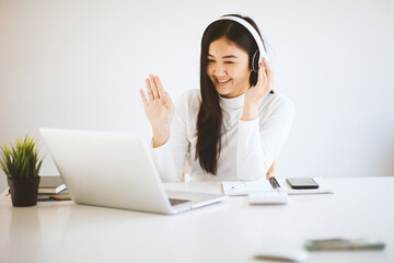 Asian young female student sitting at the laptop computer, using headphones when studying.