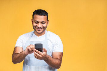 Portrait of handsome excited cheerful joyful indian african american guy cook wearing casual sending and getting messages isolated over yellow background. Using phone, finding recipe.