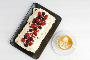 Homemade delicious meringue dessert with berries and cup of coffee cappuccino on white wooden table. Top view.