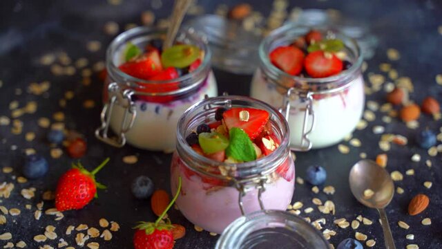 Yogurt oat muesli and fresh berries in jars rotate on a dark background. Healthy breakfast with yoghurt and fruits.
