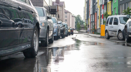 Street in a city without people with parked cars in rainy weather. Rain on the road. Rain and cars. Background of parked cars on a rainy city street. Symmetrical parked cars.