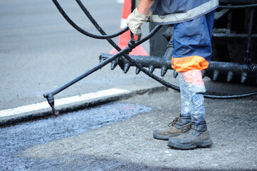 Worker lay bitumen using tar sprayer, standing in front of a bitumen spraying machine