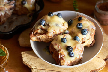Cinnamon rolls with white chocolate and blueberries. Brioche. Side view, wooden background, icing sugar, cocoa, yeast buns.