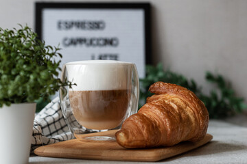 A cup of cappuccino with croissant on the table and a light background