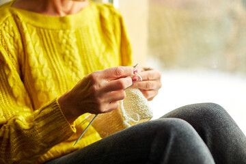 Mature female sitting on the windowsill and knitting