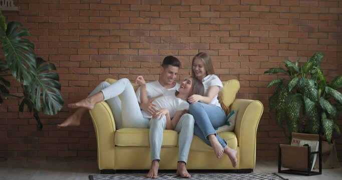 Handsome young man and two beautiful women on sofa at home. Polyamory concept