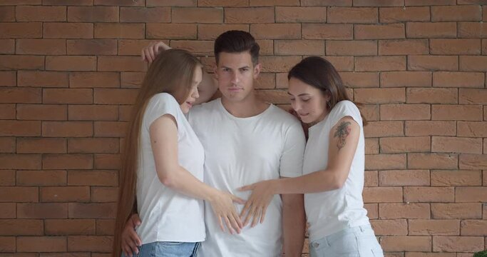 Handsome man and two beautiful women on brick background. Polyamory concept