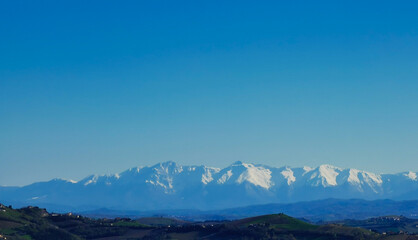 Fototapeta na wymiar Cime innevate valli e colline dei monti appennini nel cielo azzurro di una giornata primaverile
