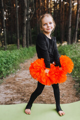 A beautiful, smiling girl, a child cheerleader in a black suit dances, performing movements, in the...