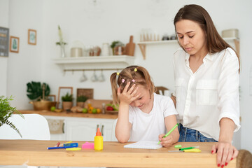 Young girl doing homework during extra-curricular classes with a tutor. Frustrated young mother or tutor teaching kid at home, remote school education. A worried young parent scolds his child. Quarrel
