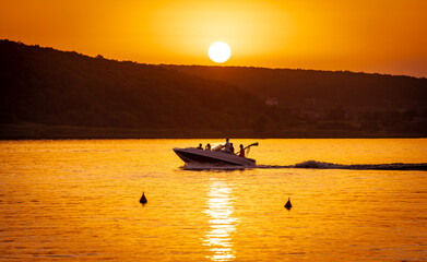 Naklejka premium Silhouette of motorboat on the river at summer sunset