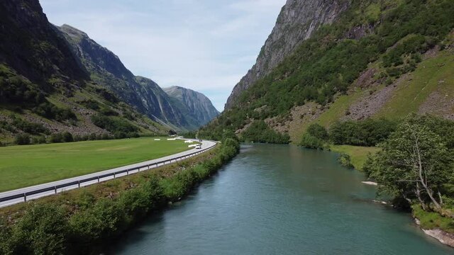 European road E39 passing through deep valley between glacial river and green farmland grass fields - Aerial slowly moving forward above river