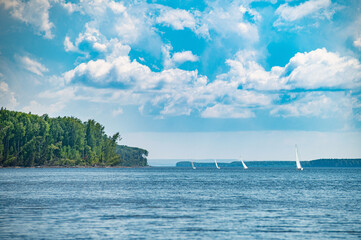 Sailing yachts sail under a beautiful sky with clouds, on the Kama River on the shore-a light fog.
