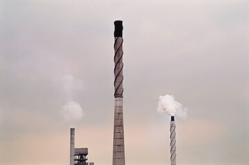 Three industrial smokestacks against moody sky..