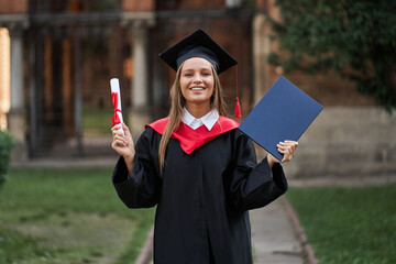Female graduate in graduation robe with diploma in her hands in campus
